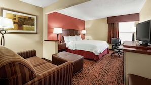 A hotel room with a bed, two bedside tables with lamps, a desk with a computer, a chair, an ottoman, and a television.