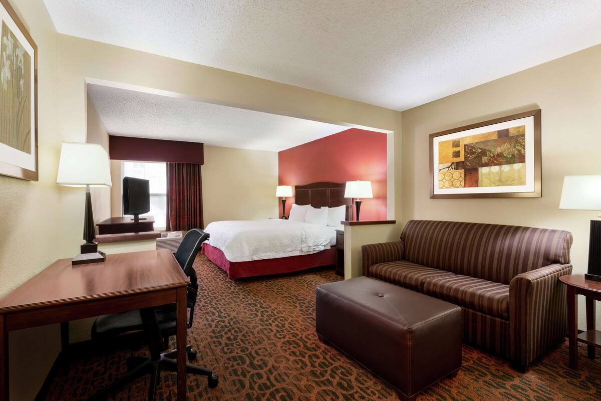 Quarto de hotel com cama, escrivaninha, cadeira, sofá e banquinho.