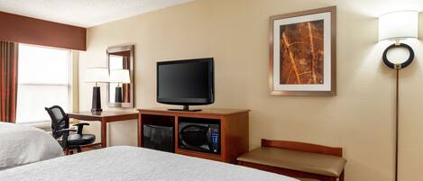 Quarto de hotel com duas camas, televisão, micro-ondas, secretária com abajur, um banco e um quadro na parede.
