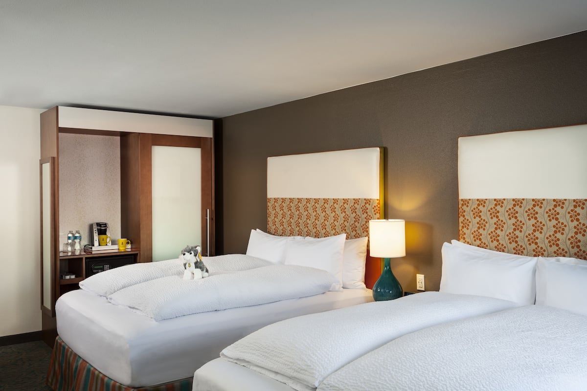 A hotel room with two beds, a desk with a coffee maker, and a lamp.