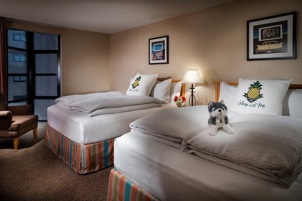 A hotel room with two beds, a chair, and a window.