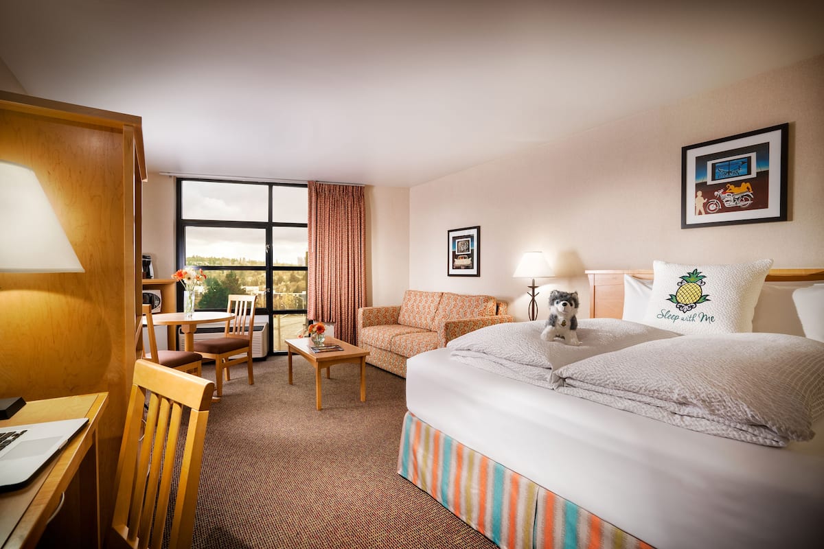 A hotel room with a bed, a desk, a chair, a sofa, and a window with curtains.