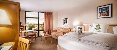 Ein Hotelzimmer mit Bett, Schreibtisch, Stuhl, einer Couch und einem Fenster mit Vorhängen.