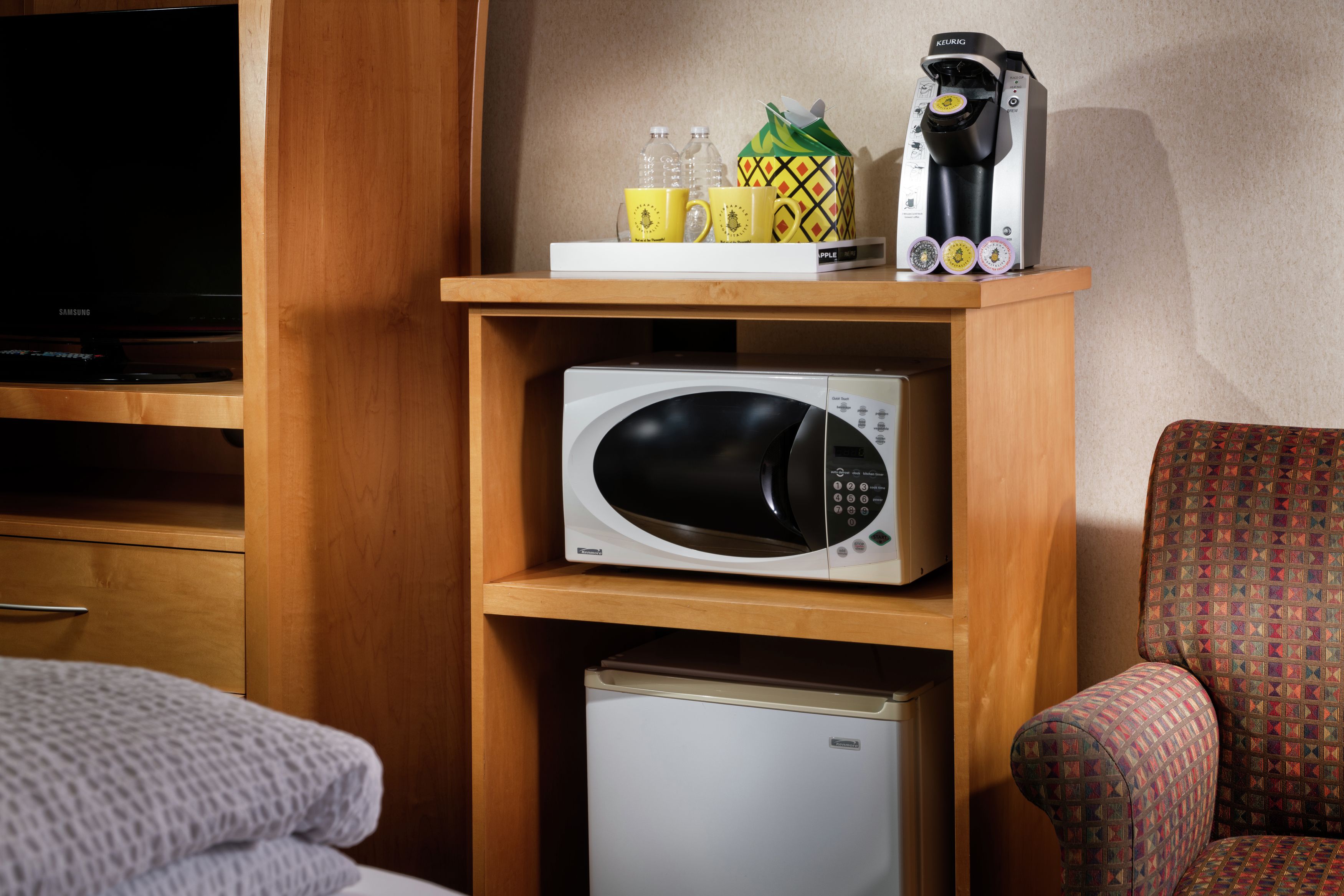 Une petite cuisine équipée comprenant un four à micro-ondes, un petit réfrigérateur et une machine à café, le tout installé sur une étagère en bois.