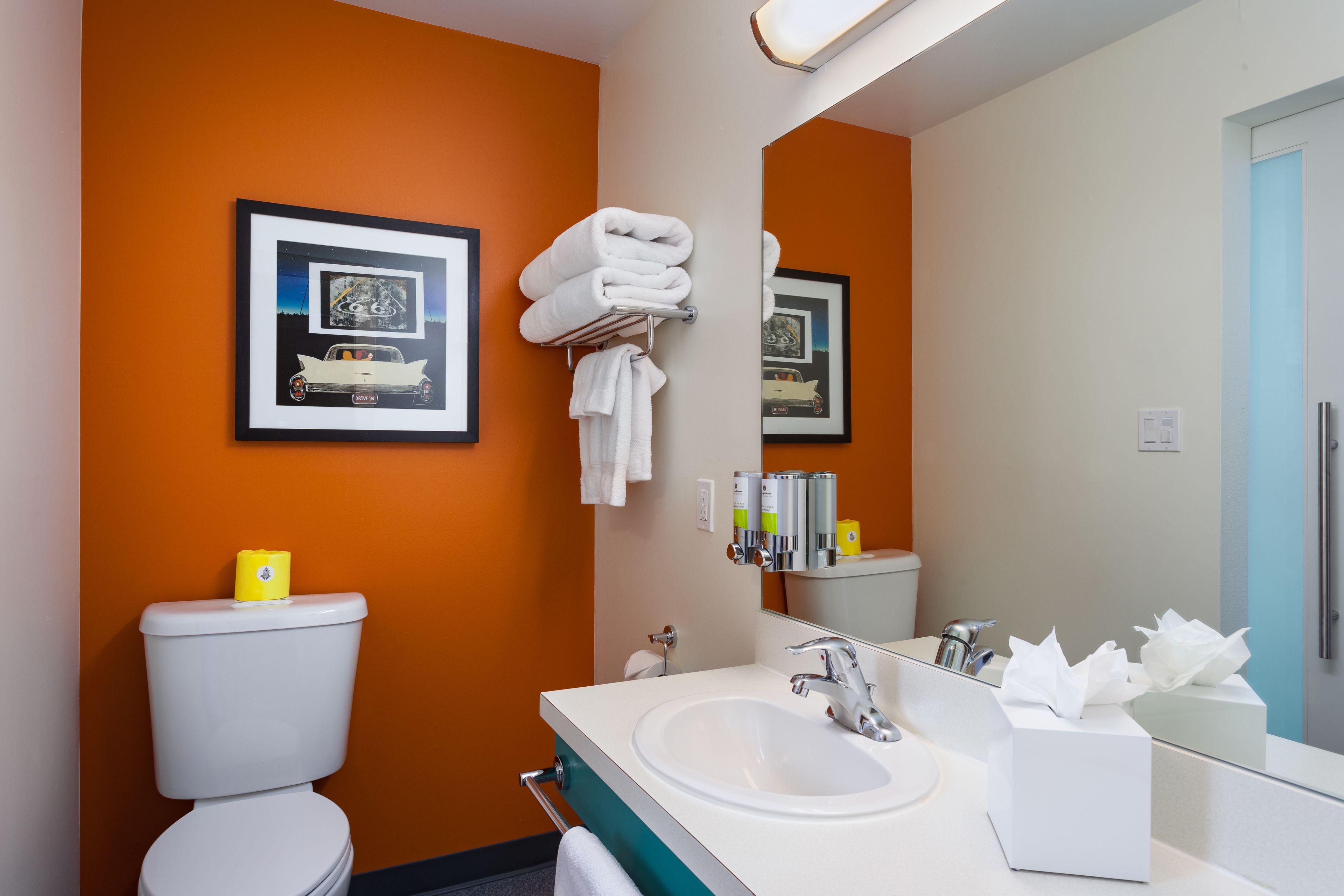 Une salle de bain avec un mur orange, un lavabo blanc, des toilettes et des tableaux encadrés accrochés au mur.