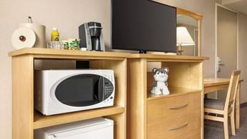Habitación de hotel con un escritorio de madera, microondas, refrigerador, televisor y un pequeño peluche.