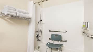 Ein Badezimmer mit Dusche, einer Haltestange, einer rollstuhlgerechten Sitzbank und einem Handtuchhalter.