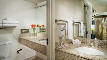 A bathroom with a granite countertop, a white sink, a towel rack, a mirror, and a toilet.