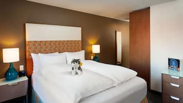 Una habitació d'hotel amb un llit gran, dues làmpades laterals, un peluix i una fotografia emmarcada a la tauleta de nit.