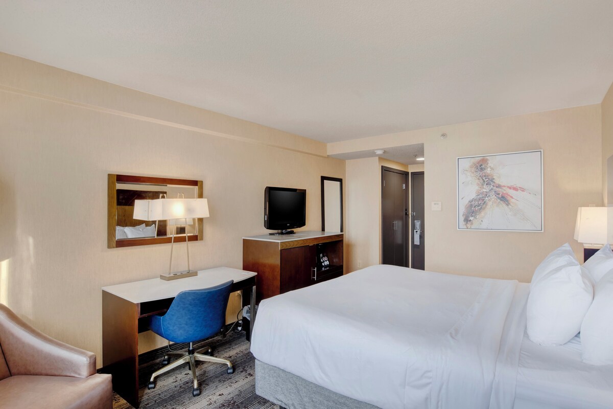 Habitación de hotel con cama, escritorio con silla, televisor, armario y un cuadro en la pared.