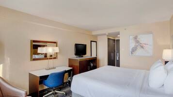 A hotel room with a bed, a desk with a chair, a television, a wardrobe, and a painting on the wall.