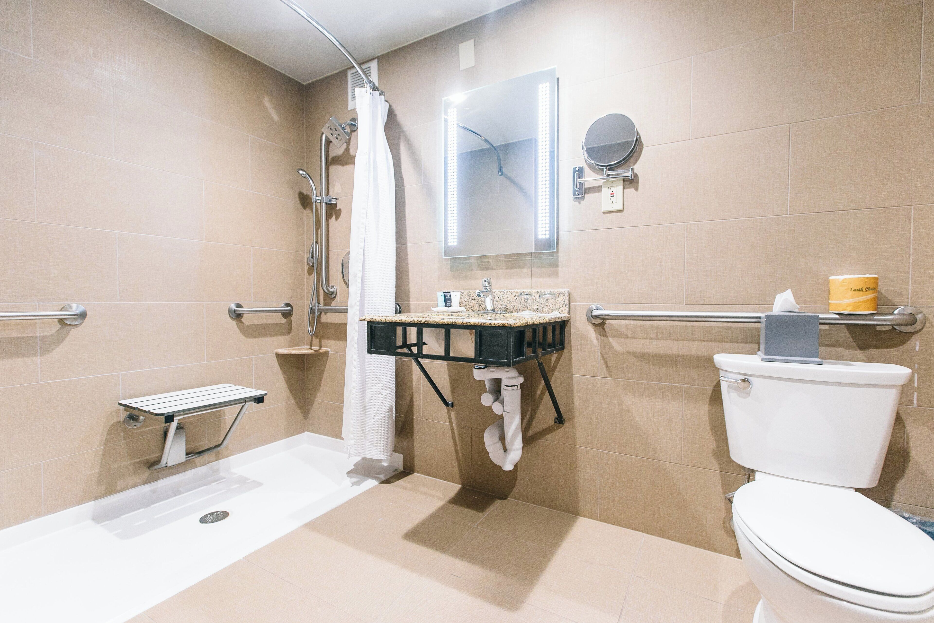 A modern bathroom with a walk-in shower, grab bars, a toilet, and a vanity with a mirror.
