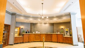 Zona de recepción de un hotel con un mostrador curvo, una lámpara moderna y suelo de baldosas.