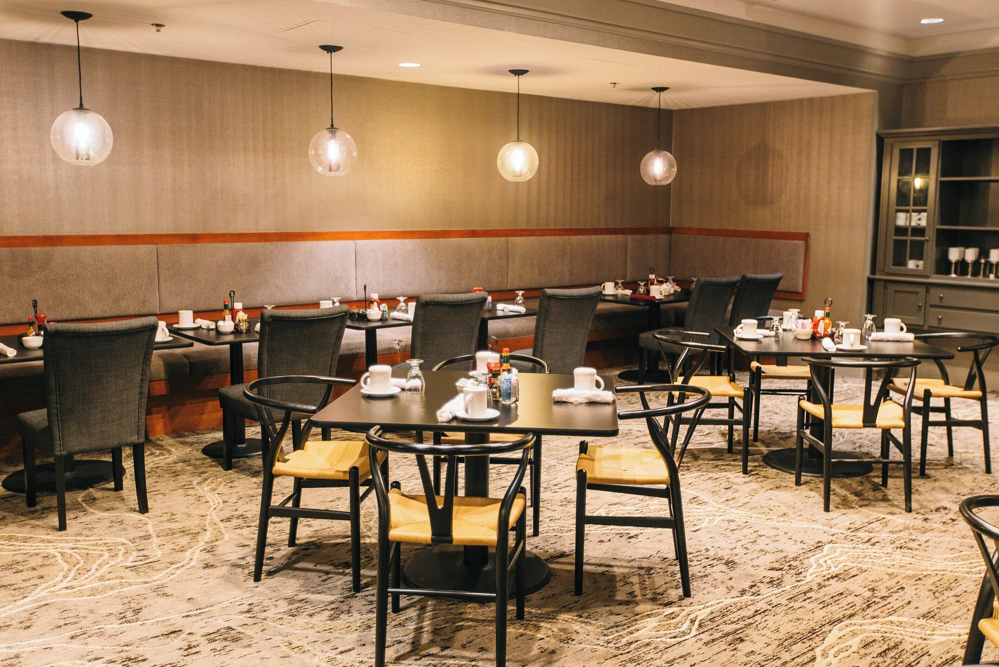 A hotel dining area with multiple tables and chairs, equipped with table settings and beverage dispensers.