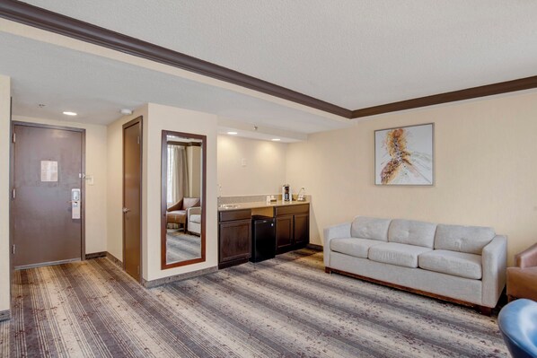 Una habitación de hotel con piso de madera, un sofá, una zona de cocina y una puerta.