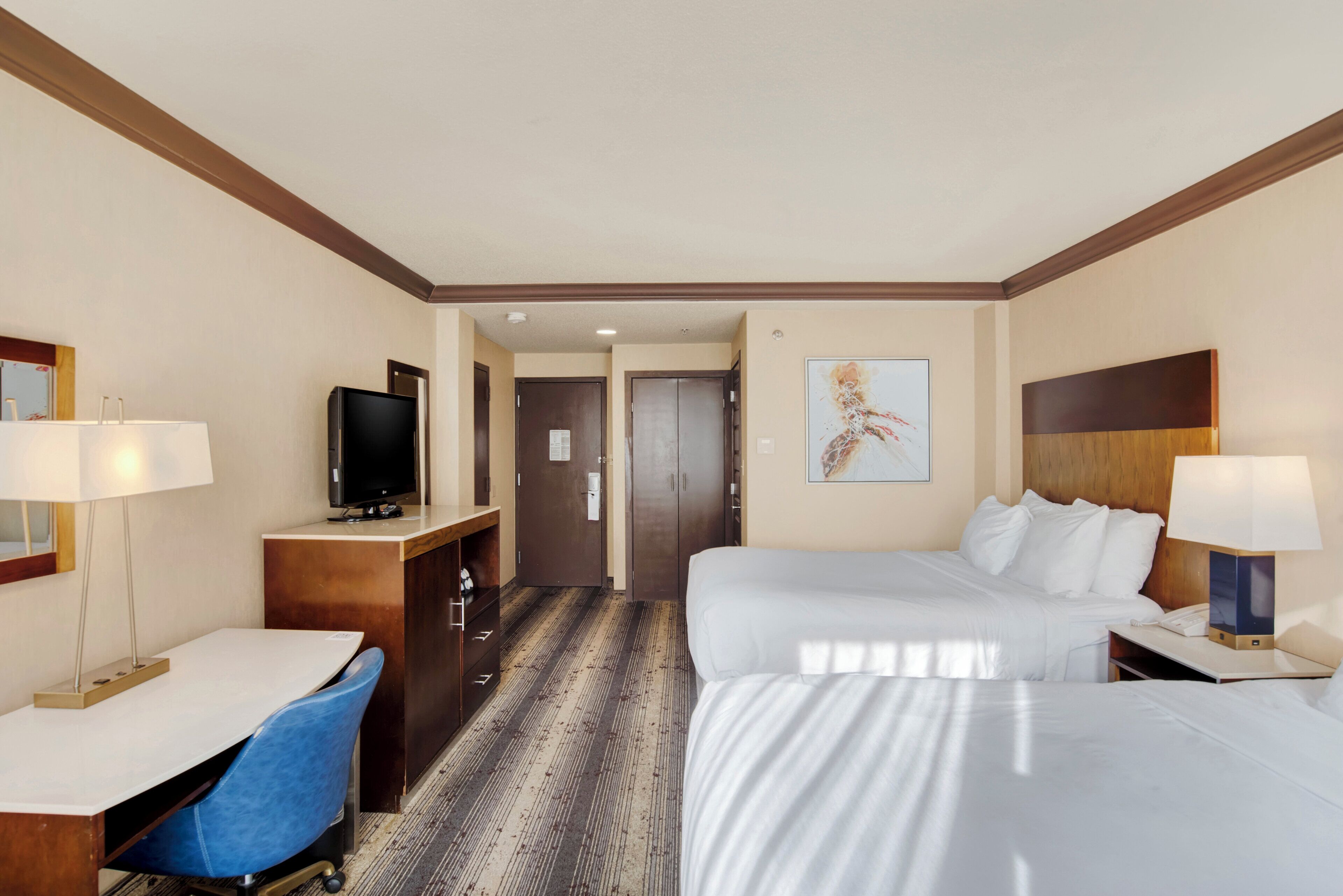 A hotel room with a bed, desk, chair, television, and artwork on the wall.