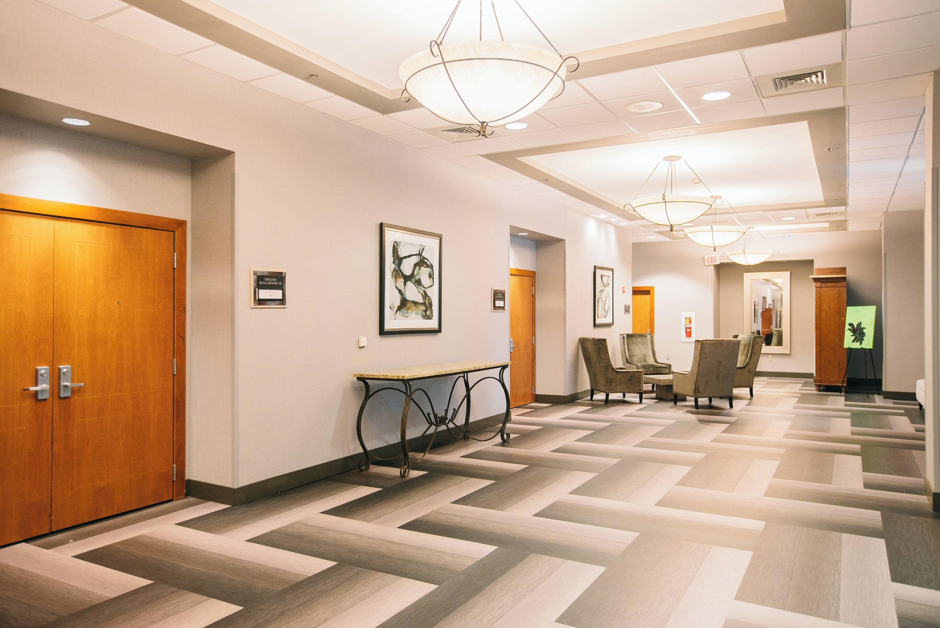 A hotel hallway with a checkered floor pattern, wooden doors, and a seating area with a table and chairs.