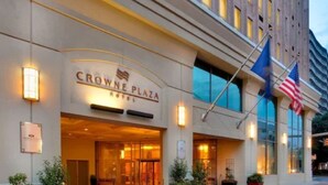 Exterior del Hotel Crowne Plaza con una entrada destacada, banderas estadounidenses y plantas en macetas.