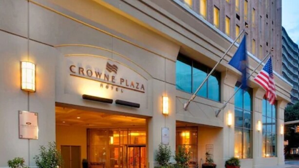 Exterior del Hotel Crowne Plaza con una entrada destacada, banderas estadounidenses y plantas en macetas.
