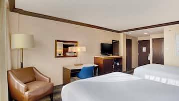 A hotel room with two beds, a desk with a chair, a television, and a lamp.