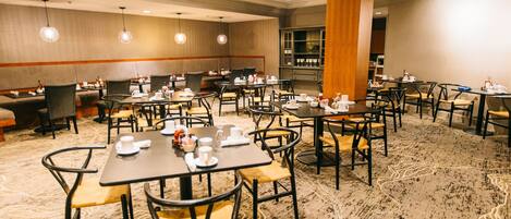A hotel dining area with multiple tables and chairs, equipped with table settings and a large wooden pillar.