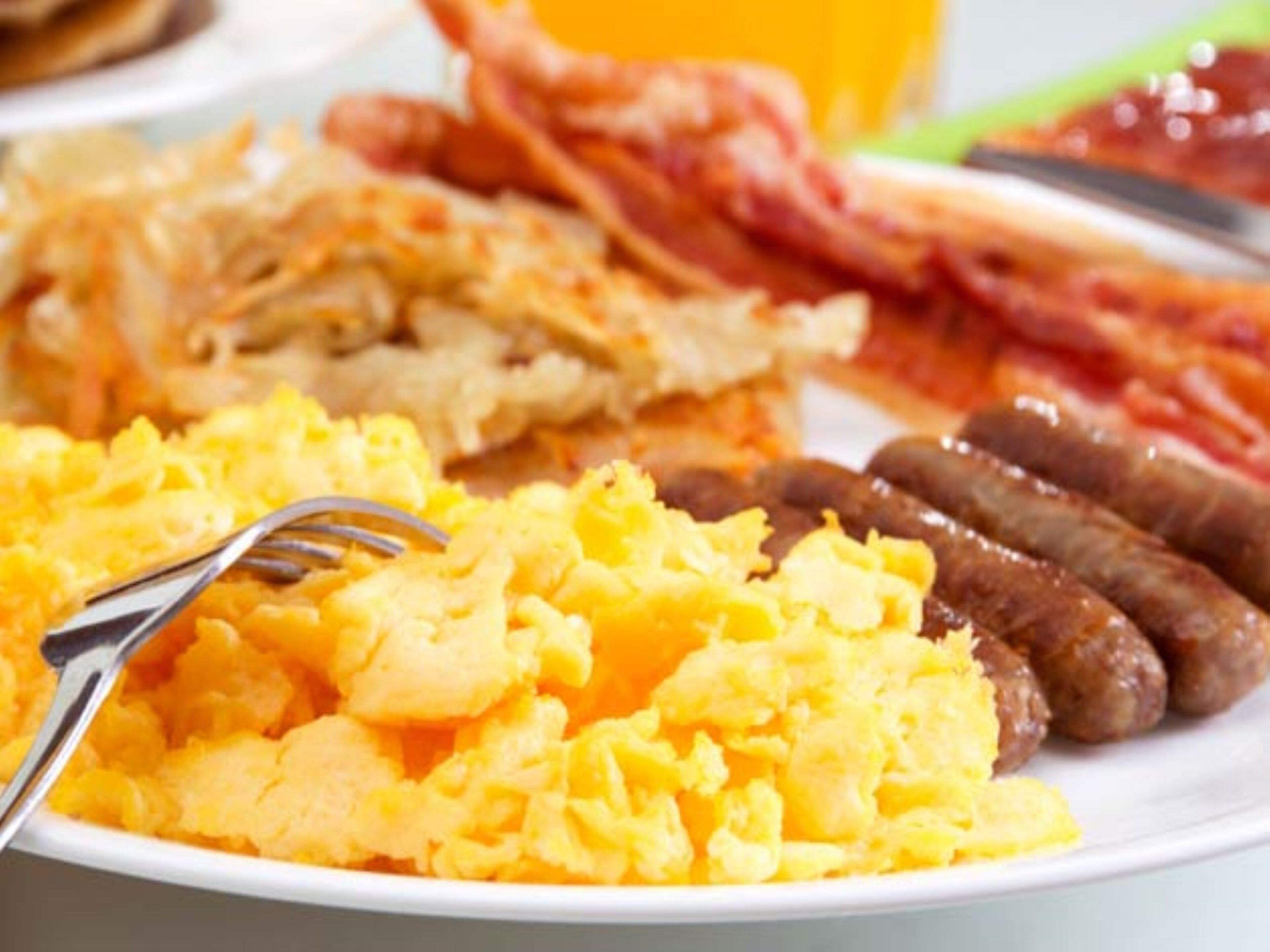 A plate of scrambled eggs, sausages, and bacon.