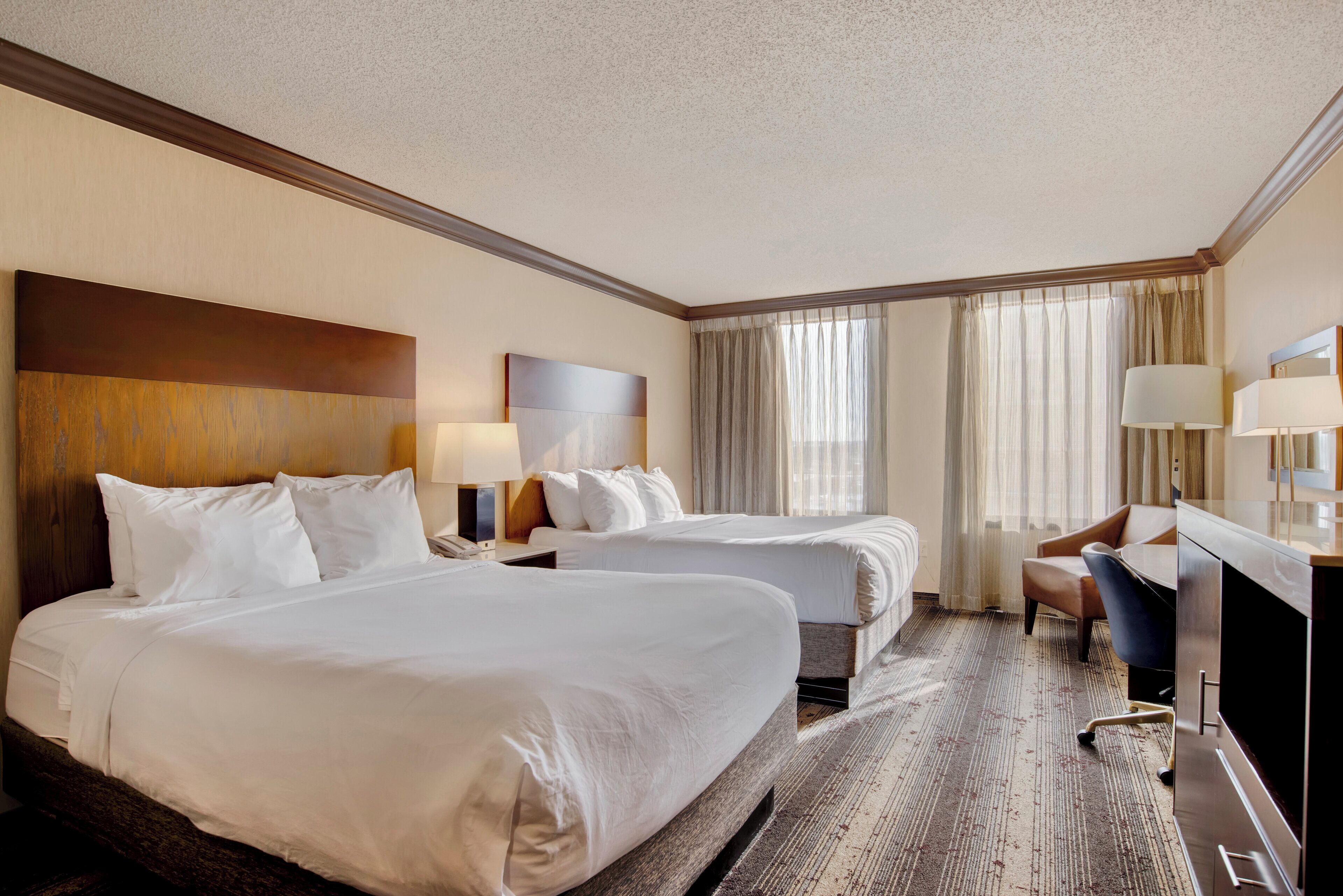 Une chambre d’hôtel avec deux lits, un bureau, une chaise et un téléviseur.
