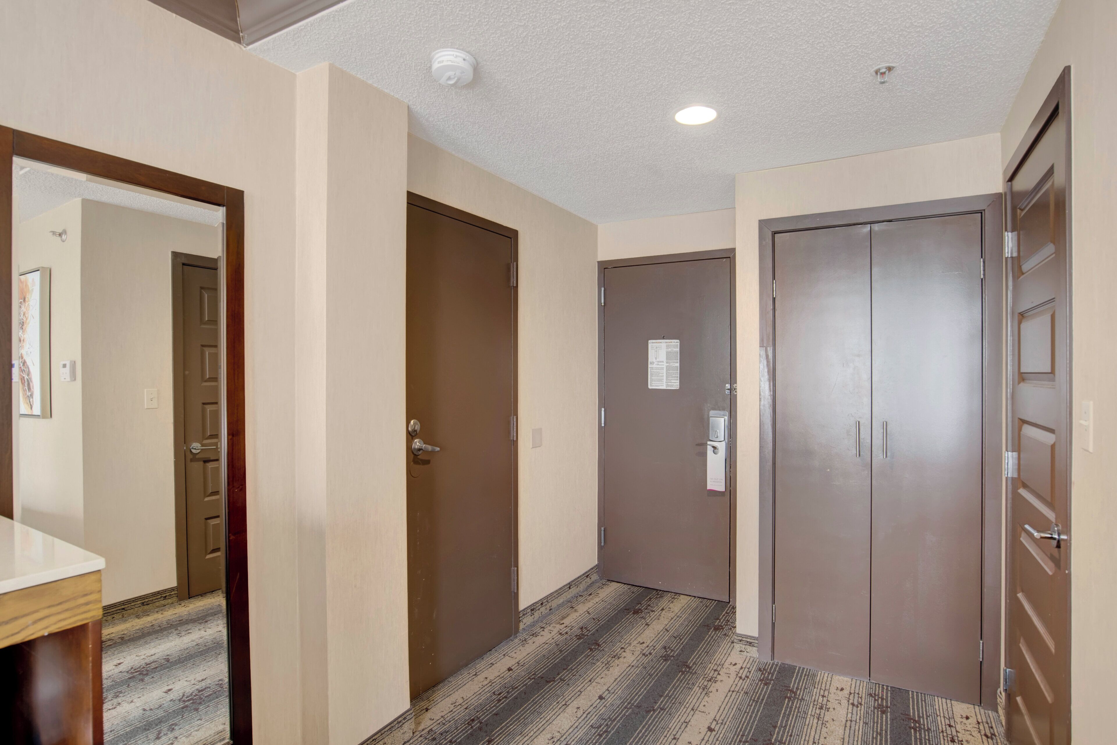 Un couloir avec trois portes, un banc en bois et un luminaire au plafond.