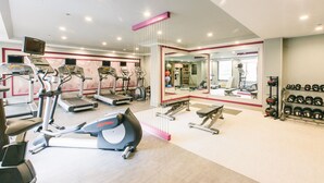 Un gimnasio con cintas de correr, elípticas, una prensa de banca y un estante con mancuernas.