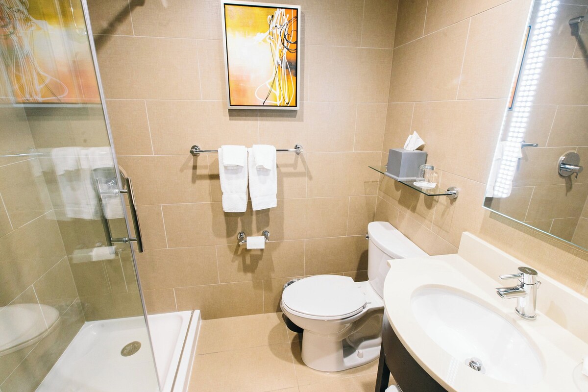 Un baño moderno con cabina de ducha de vidrio, inodoro blanco, lavamanos con espejo y azulejos color beige.