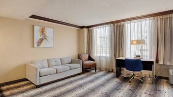 Habitación de hotel con sofá, una silla, escritorio y lámpara.