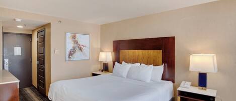 A hotel room with a large bed, two bedside tables with lamps, a desk, and a door.