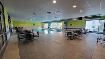 An indoor swimming pool area with tiled flooring, multiple seating areas, and large windows providing natural light.