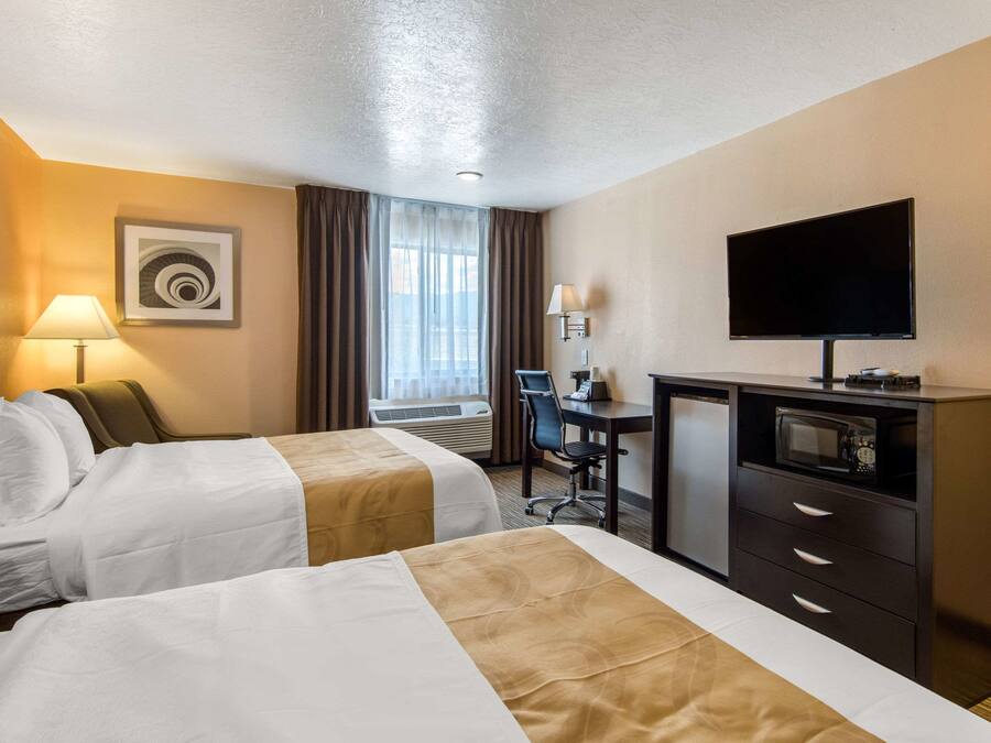 Una habitación de hotel con dos camas, un escritorio con computadora, televisión y microondas.
