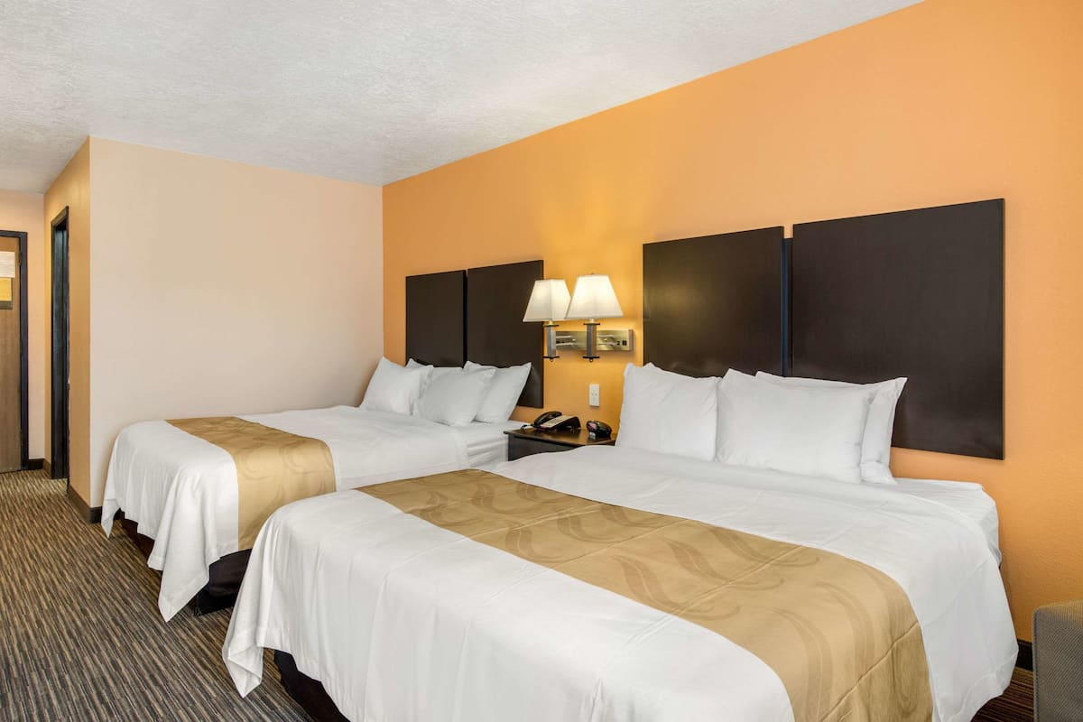 A hotel room with two beds, a nightstand with a lamp, and a wall-mounted phone.