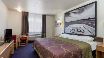Habitación de hotel con cama, escritorio con televisor, silla, ventana con cortinas e imagen de una carretera en la pared.