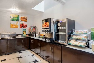Una cocina con muebles oscuros, una estación de café, un refrigerador y una vitrina con sándwiches.