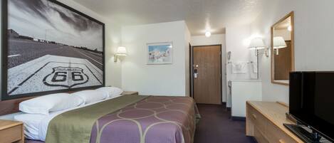 Habitación de hotel con cama, escritorio con televisor, un cuadro grande de una carretera y puerta que da a un baño.