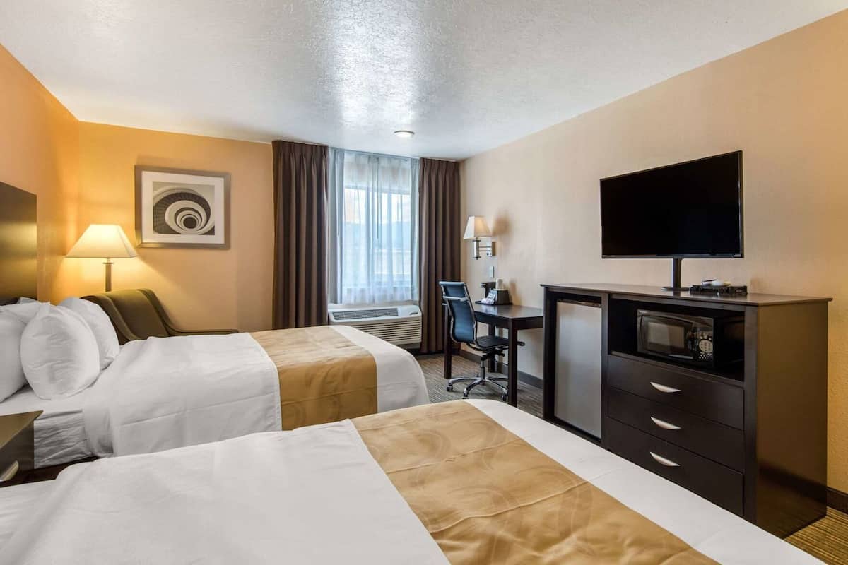 A hotel room with two beds, a desk, a television, and a minibar.