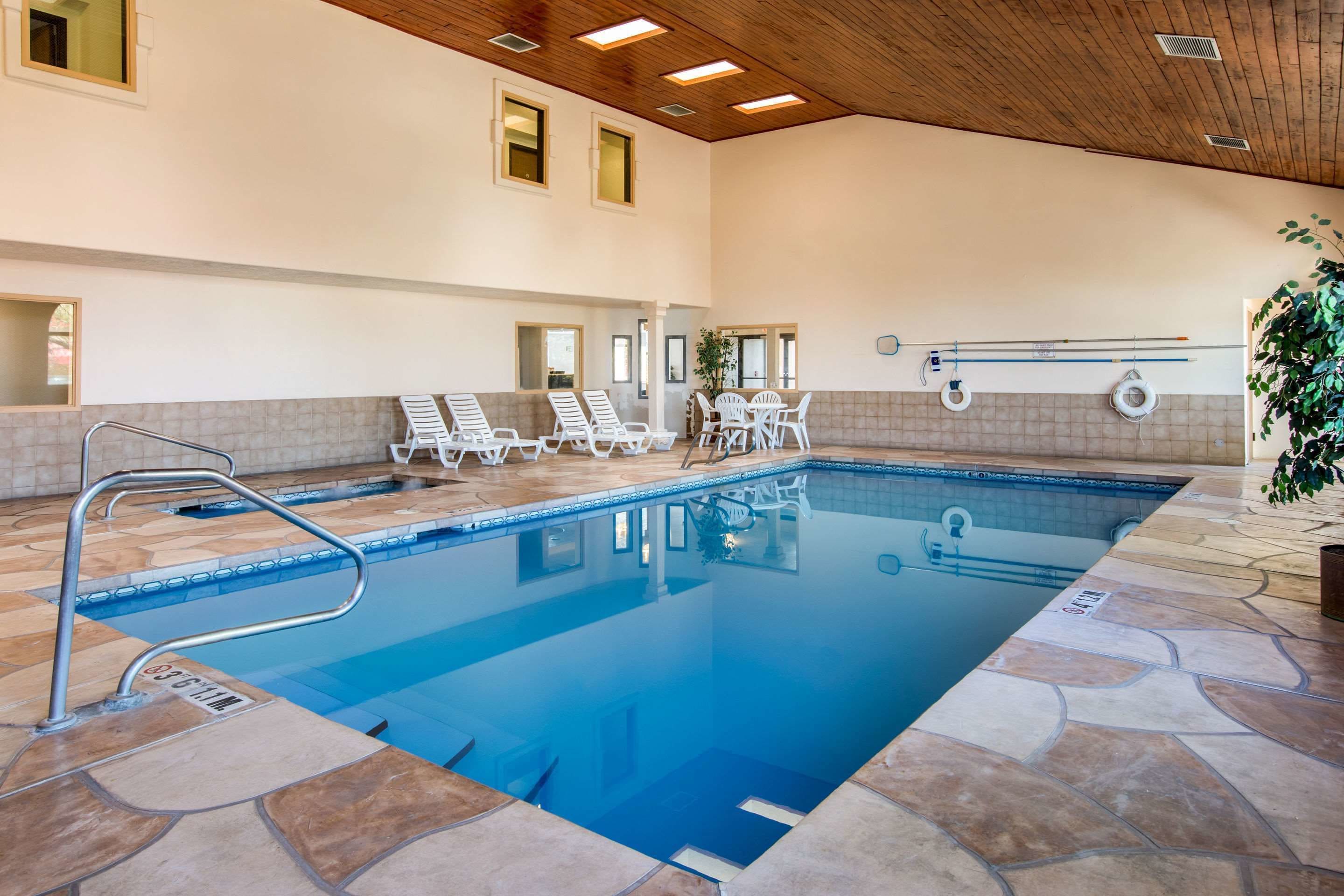 An indoor swimming pool with clear water, surrounded by stone tiles, and equipped with a lifeguard stand and lounge chairs.