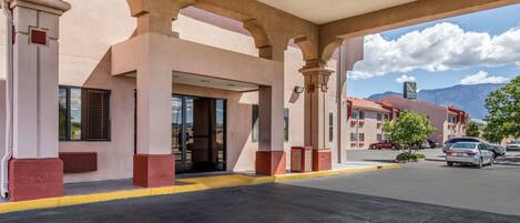 A hotel entrance with a covered outdoor area, large windows, and a view of mountains in the background.