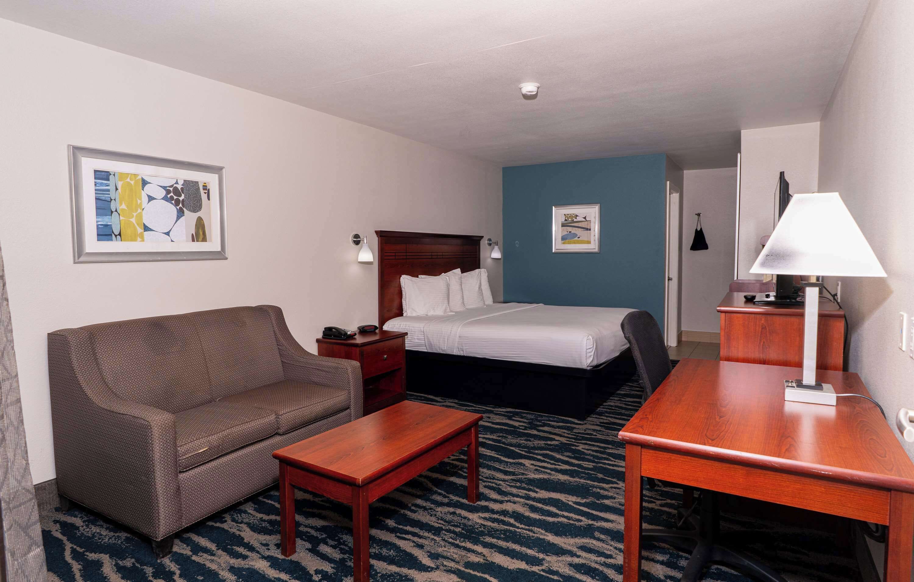 Quarto de hotel com cama, sofá, escrivaninha e abajur.