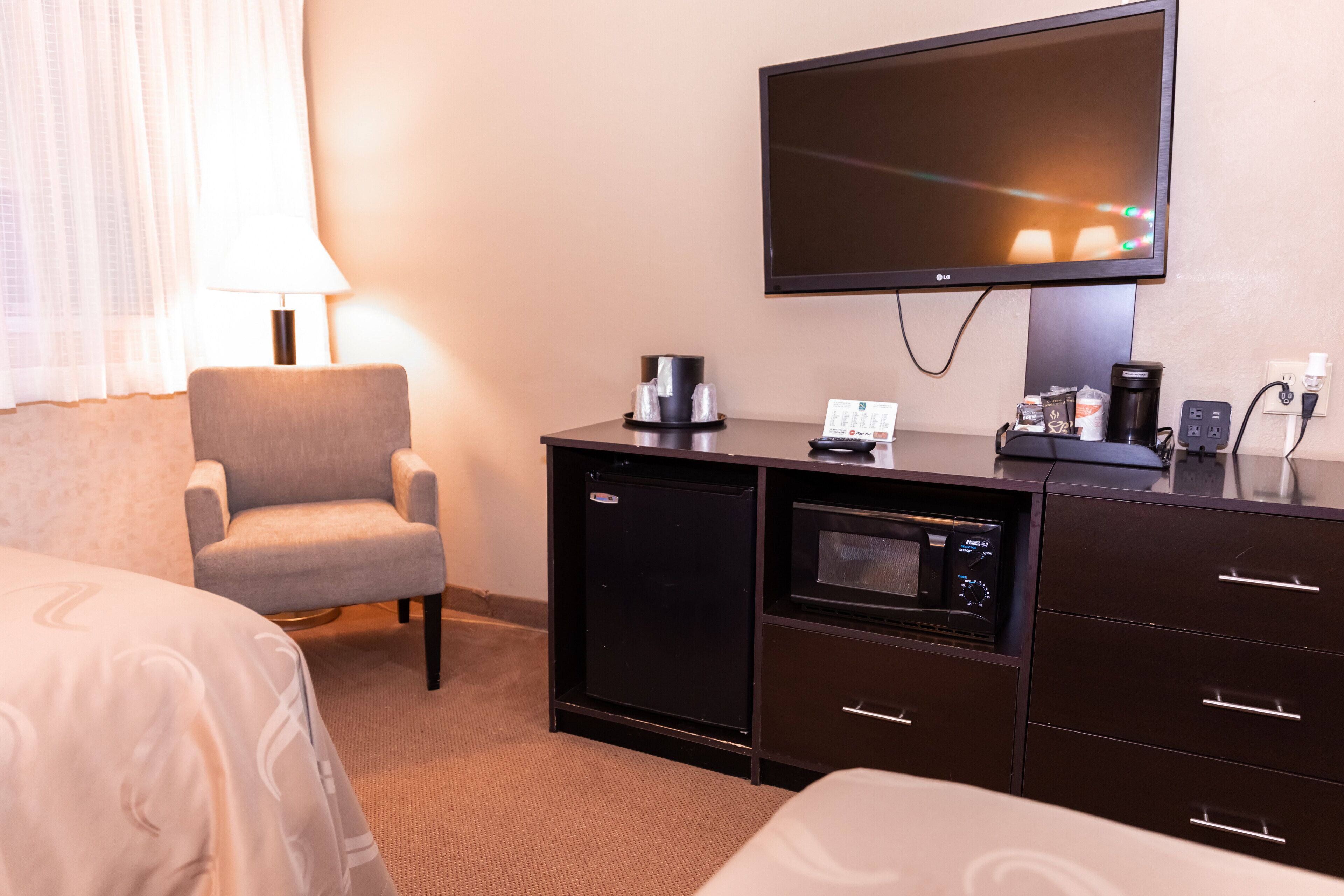 A hotel room with a bed, a chair, a desk with a coffee maker, a television, and a small refrigerator.