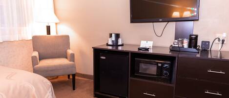 A hotel room with a bed, a chair, a desk with a coffee maker, a television, and a small refrigerator.