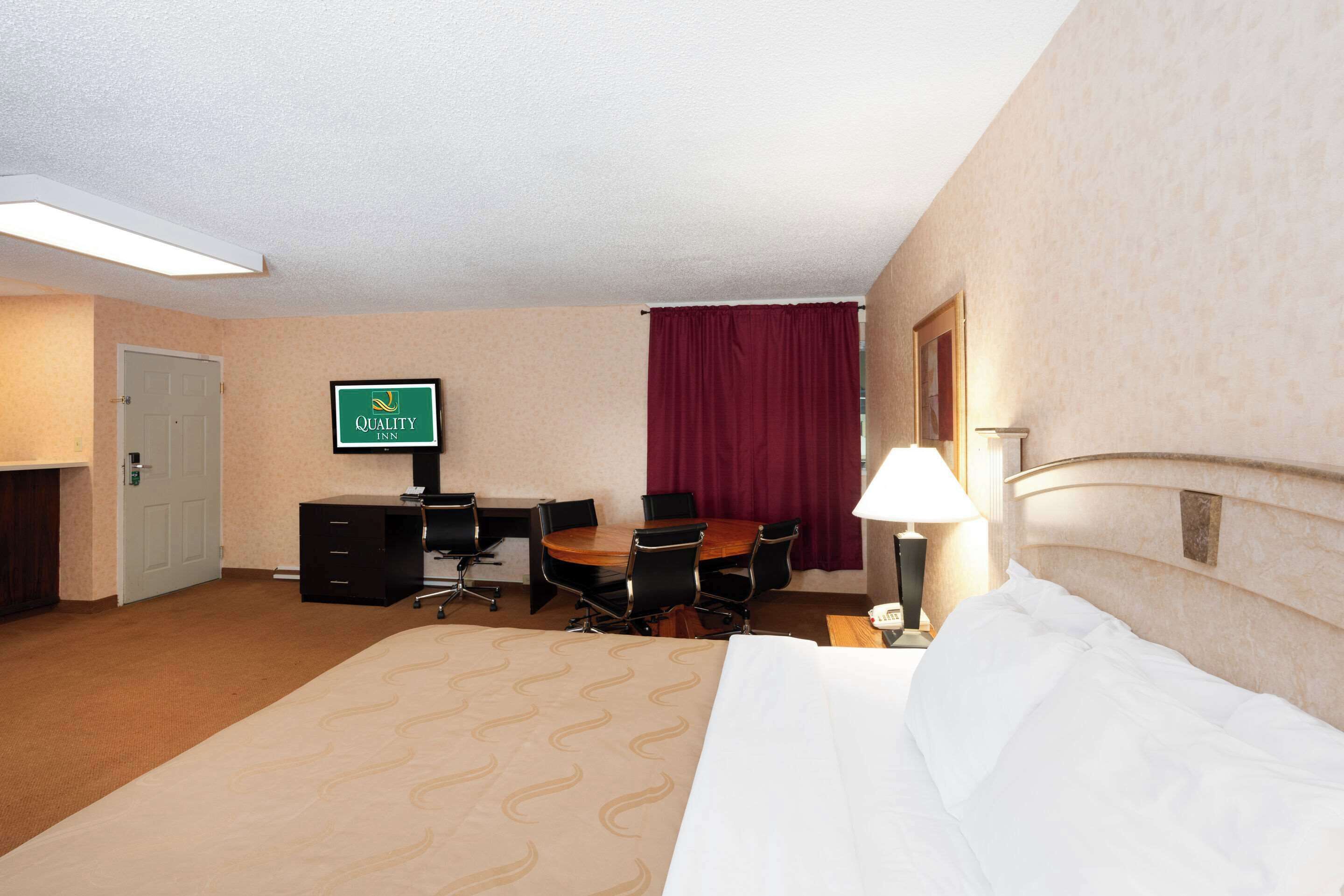 A hotel room with a bed, a desk with a chair, a television, and a lamp.