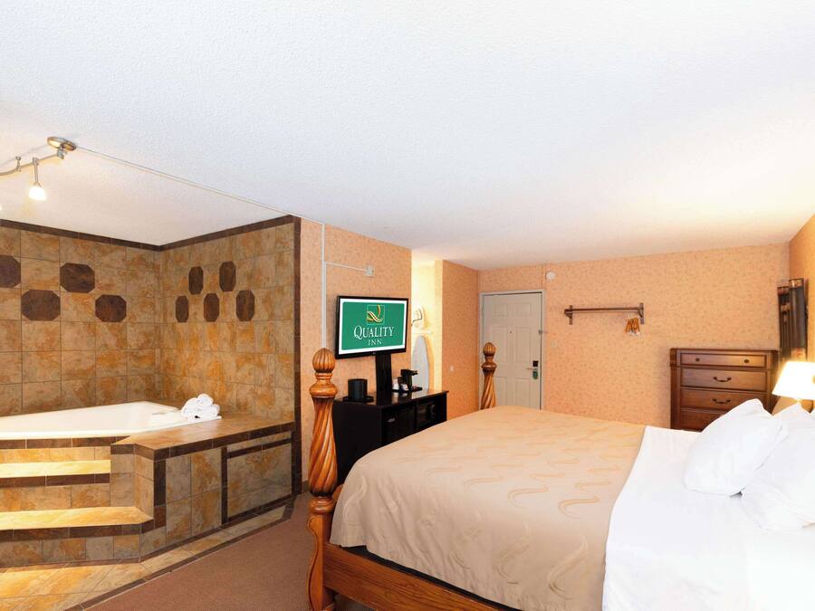 A hotel room with a bathtub, a bed, a desk, and a television displaying the hotel name.
