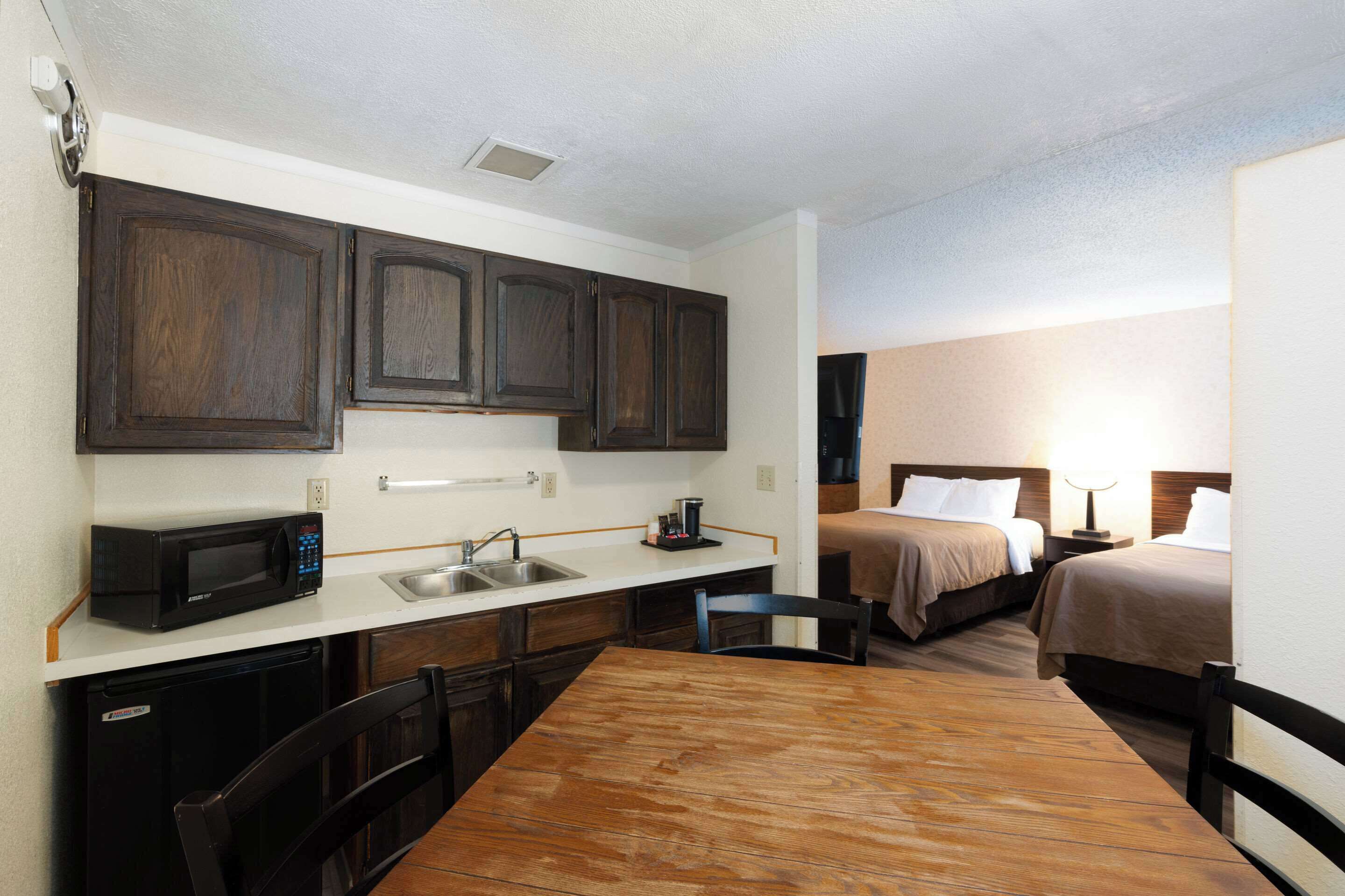 Una habitación de hotel compacta con kitchenette, una mesa de comedor, dos camas y un baño pequeño.