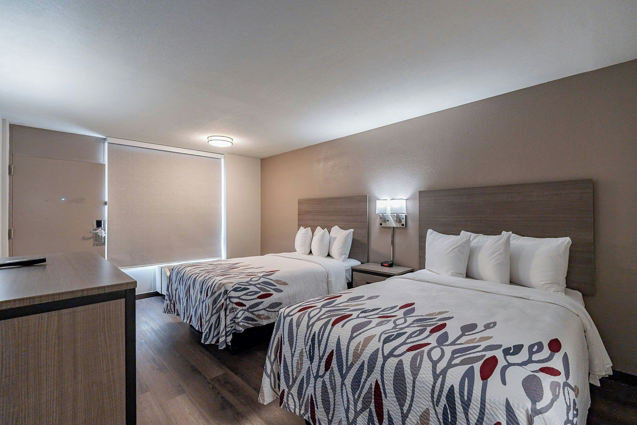 A hotel room with two beds, a desk, and a door.