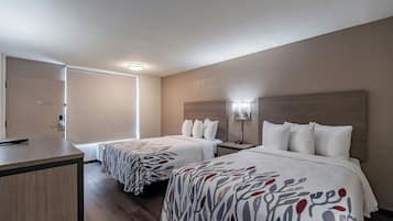 A hotel room with two beds, a desk, and a door.