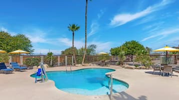 A swimming pool with lounge chairs and umbrellas, surrounded by a fence and palm trees.